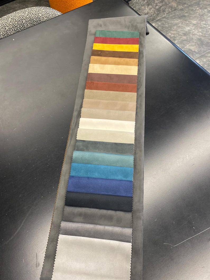 May include: A fabric swatch card featuring a variety of colors. The card displays rectangular fabric samples in shades of green, red, yellow, brown, beige, blue, and gray. The samples are arranged vertically on a gray backing.