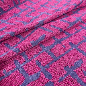 Könnte beinhalten: Nahaufnahme eines strukturierten Stoffes mit geometrischem Muster. Der Stoff hat eine leuchtende Fuchsiafarbe mit einem kontrastierenden marineblauen Design. Das Muster besteht aus miteinander verbundenen Quadraten und Linien und erzeugt einen modernen und auffälligen Textil.
