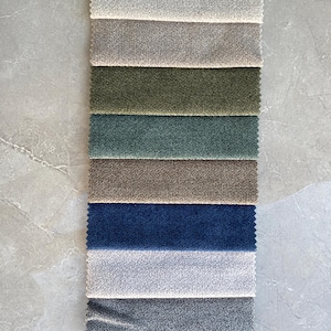 Op de afbeelding: Een verticale weergave van stofstalen in diverse kleuren, waaronder bordeaux, cr&egrave;me, grijs, olijfgroen, blauwgroen, bruin, marineblauw, lichtgrijs en antraciet. De stalen hebben een getextureerd uiterlijk, waarschijnlijk voor bekleding of interieurdecoratie.