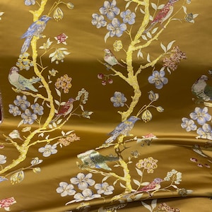 May include: Gold-colored fabric with a repeating pattern of birds perched on flowering branches. The birds are in shades of blue, red, and green, with the branches in gold. The flowers are in shades of blue, pink, and white.