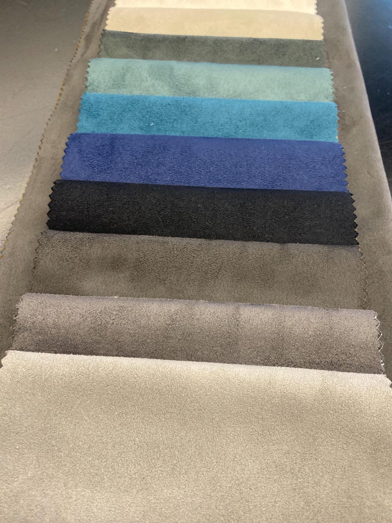 May include: A selection of fabric swatches in various colors, including beige, gray, teal, blue, and black. The samples are arranged in a row, showcasing the different textures and shades available for upholstery or design projects.