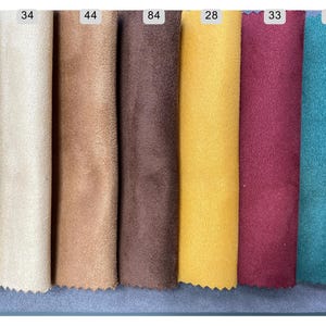 May include: A collection of fabric swatches in various colors, including purple, cream, tan, brown, yellow, burgundy, and teal. Each swatch is labeled with a number, showcasing a range of textures and hues for design and crafting purposes.
