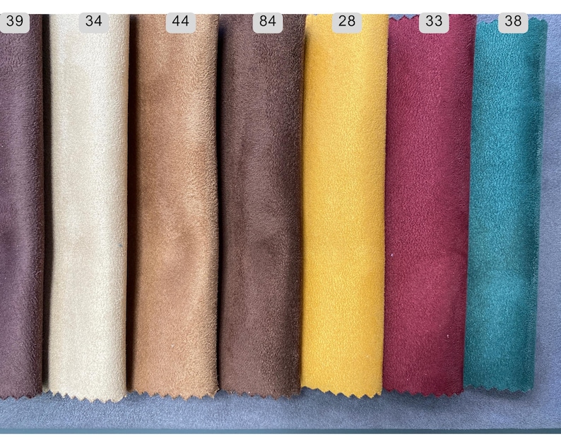 May include: A collection of fabric swatches in various colors, including purple, cream, tan, brown, yellow, burgundy, and teal. Each swatch is labeled with a number, showcasing a range of textures and hues for design and crafting purposes.