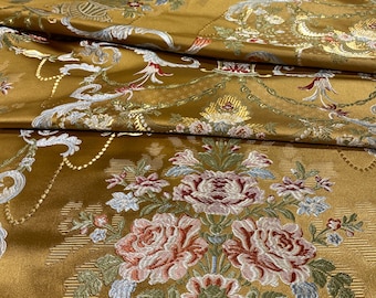 May include: Close-up of a golden-yellow brocade fabric with an ornate floral pattern. The design features large bouquets of roses in shades of red, pink, and white, along with smaller flowers and foliage in green and blue. The fabric has a luxurious sheen.