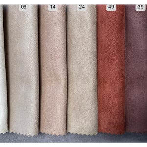 May include: A color palette of suede fabric swatches in various shades. The swatches include off-white, beige, light brown, tan, rust, and deep burgundy. Each swatch is labeled with a number at the top. The fabric has a soft, textured appearance.