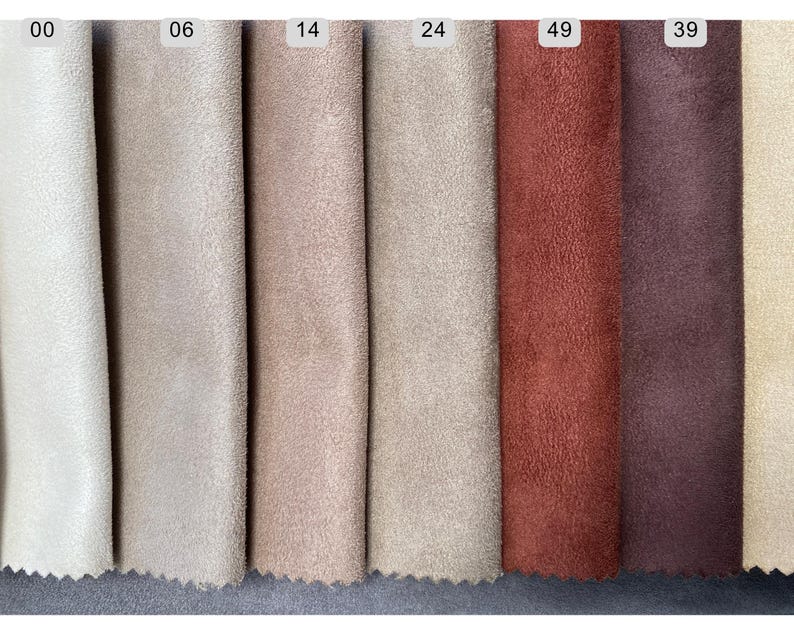 May include: A color palette of suede fabric swatches in various shades. The swatches include off-white, beige, light brown, tan, rust, and deep burgundy. Each swatch is labeled with a number at the top. The fabric has a soft, textured appearance.