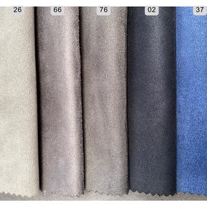 May include: Close-up of fabric swatches in various colors. The swatches include shades of gray, blue, and teal. Each swatch has a number printed on it. The fabric has a soft, suede-like texture.