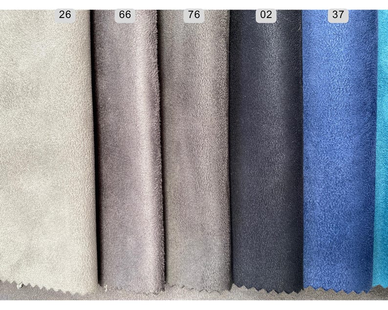 May include: Close-up of fabric swatches in various colors. The swatches include shades of gray, blue, and teal. Each swatch has a number printed on it. The fabric has a soft, suede-like texture.