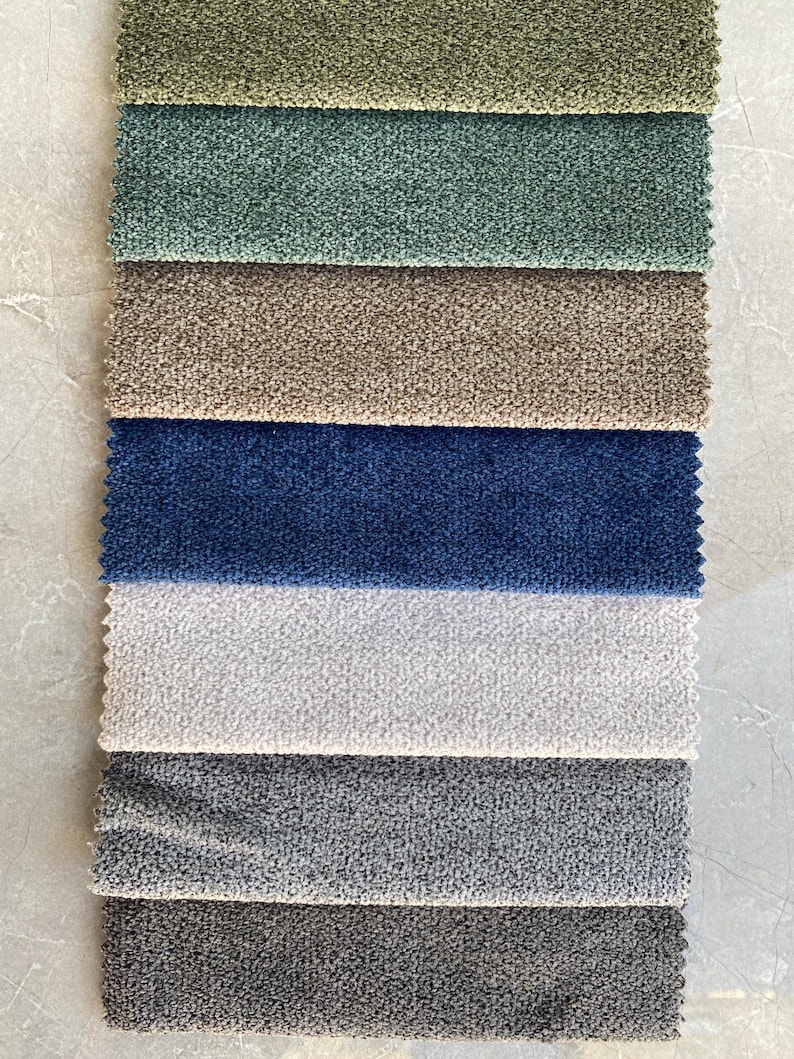 Op de afbeelding: Een verticale weergave van stofstalen in verschillende kleuren. De stalen omvatten tinten groen, blauw, bruin en grijs. De stoffen hebben een getextureerde, geluste uitstraling, wat wijst op een pluche of boucl&eacute; materiaal, geschikt voor bekleding of interieurdecoratie.