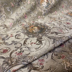 Peut inclure: Gros plan sur un tissu vert olive luxueux avec un motif floral orné. Le design comprend des médaillons ovales avec des compositions florales, entourés de volutes et de petites fleurs roses. Le tissu a une texture douce et veloutée.