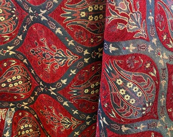 May include: Close-up of a red fabric with an intricate pattern. The design features floral and geometric shapes in gold, black, and dark red. The fabric has a textured appearance, suggesting a woven material, possibly for upholstery or drapery.