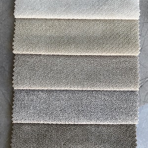 Op de afbeelding: Een verticale presentatie van stofstalen in diverse neutrale kleuren. De stalen vari&euml;ren van lichtcr&egrave;me tot donkergrijs en mosterdgeel. Elke staal heeft een getextureerd, gelust oppervlak, ideaal voor bekleding.