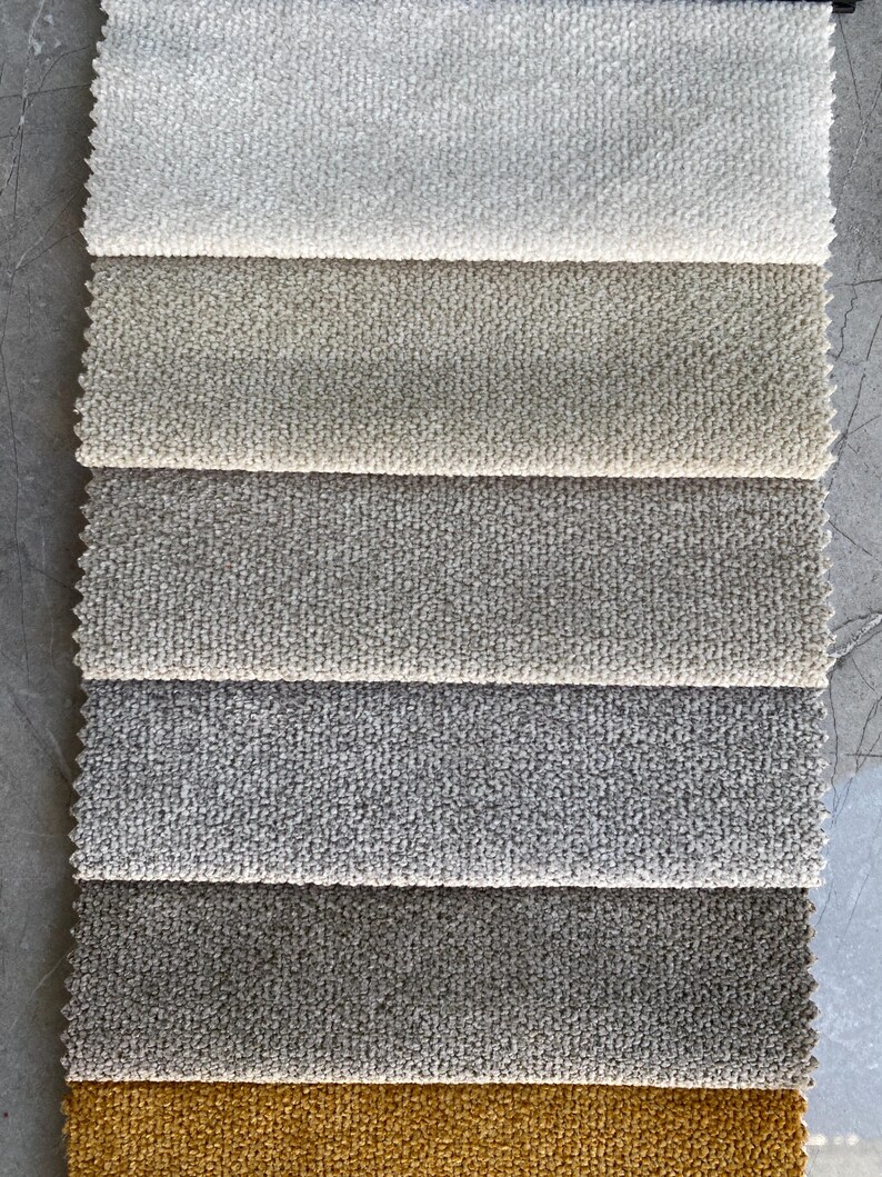 Op de afbeelding: Een verticale presentatie van stofstalen in diverse neutrale kleuren. De stalen vari&euml;ren van lichtcr&egrave;me tot donkergrijs en mosterdgeel. Elke staal heeft een getextureerd, gelust oppervlak, ideaal voor bekleding.