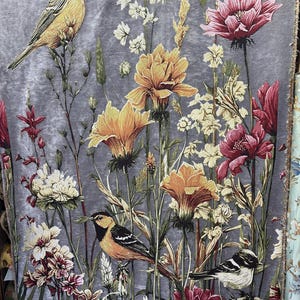 Könnte beinhalten: Grauer Stoff mit einem Blumen- und Vogelmuster. Das Design umfasst gelbe, orangefarbene und burgunderfarbene Blumen sowie mehrere Vögel. Der Hintergrund ist eine gedämpfte graue Farbe. Das Design ist detailliert und auf den Stoff gedruckt.