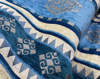 May include: Close-up of a folded fabric with a repeating pattern of blue, teal, and beige stripes. The design includes geometric shapes and textured details, creating a layered effect. The fabric appears soft and plush.