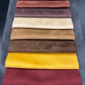 May include: A collection of fabric swatches in various colors, including beige, brown, and burgundy. The samples are arranged in a vertical stack, showcasing the different textures and shades of the material. The swatches are likely for upholstery or interior design.