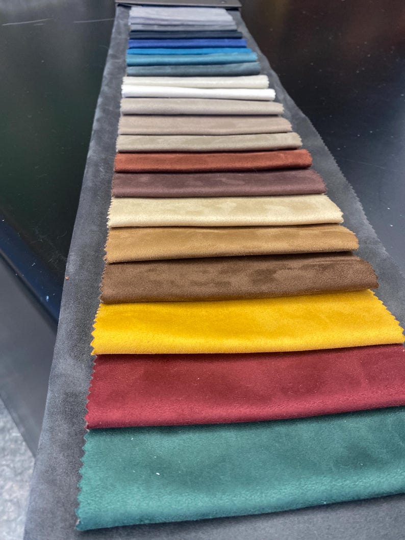May include: A fabric swatch card featuring a variety of colors. The samples include shades of gray, blue, beige, brown, yellow, red, and green. The fabric appears to be a soft, velvety material, ideal for upholstery or textile projects.