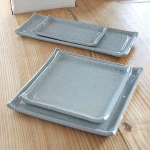 May include: Four grey ceramic square plates stacked on top of each other. The plates have a crackled glaze finish.
