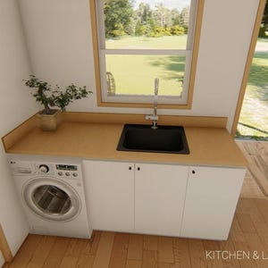May include: Interior view of a kitchen and laundry area. Features a white washing machine, white cabinets, a black sink, and a wooden countertop. A small potted plant sits on the countertop. The room has a window and a door leading to an outdoor area.