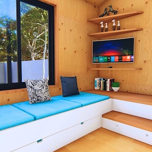 Puede incluir: Interior de una sala de estar moderna con un banco incorporado con cojines azules y cajones de almacenamiento blancos. Un televisor de pantalla plana est&aacute; montado en una pared con paneles de madera, con estantes flotantes arriba y abajo. Una gran ventana ofrece una vista del exterior.