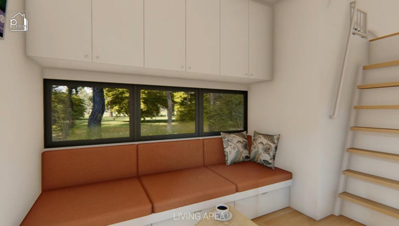 Puede incluir: Vista interior de una peque&ntilde;a sala de estar con un sof&aacute; naranja empotrado debajo de una ventana grande. Dos cojines decorativos descansan sobre el sof&aacute;. Hay armarios blancos encima de la ventana y una escalera de madera conduce a un nivel superior.