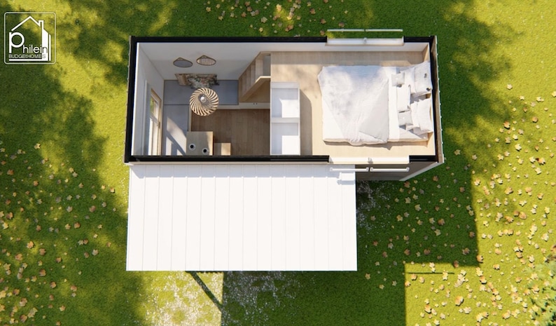 May include: An overhead view of a tiny house with a white exterior and a black roof. The interior features a bedroom with a bed, a kitchen area, and a living space. The house is surrounded by green grass and a few leaves.
