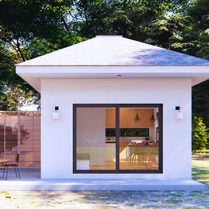 May include: A modern, white house with a gabled roof and large sliding glass doors. The interior is visible, showcasing a kitchen and dining area. Exterior features include a patio, wooden fence, and two wall-mounted lights. Lush green trees provide a natural backdrop.