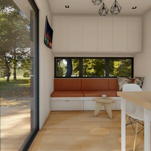 Puede incluir: Vista interior de un espacio habitable moderno con una gran ventana que da a una zona exterior verde. La habitaci&oacute;n cuenta con un banco empotrado con cojines naranjas, una peque&ntilde;a mesa de madera y una silla blanca. Arriba, hay luces colgantes decorativas.