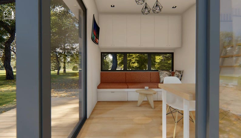 Puede incluir: Vista interior de un espacio habitable moderno con una gran ventana que da a una zona exterior verde. La habitaci&oacute;n cuenta con un banco empotrado con cojines naranjas, una peque&ntilde;a mesa de madera y una silla blanca. Arriba, hay luces colgantes decorativas.