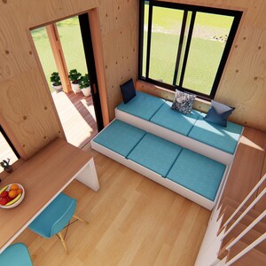 Puede incluir: Vista interior de una casa peque&ntilde;a moderna con paneles de madera clara. Incluye una peque&ntilde;a zona de cocina con mesa y sillas, una zona de estar integrada con cojines azules y una escalera. Un televisor est&aacute; montado en la pared.