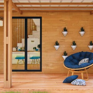 Puede incluir: Un porche exterior acogedor con una terraza y paredes de madera. Una puerta negra est&aacute; a la izquierda, y una puerta de cristal revela un vistazo del interior. Una silla papasan azul con cojines se encuentra cerca de la pared con macetas colgantes.