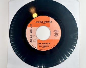 May include: A black vinyl record with a red and white label. The label features the text "Wiggle Wobble (L. Cooper)" and "Les Cooper and the Soul Rockers 5019".