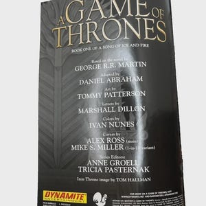 Może przedstawiać: Okładka książki "Gra o Tron" z tytułem w złotych literach. Wymienia George'a R.R. Martina jako autora i innych wsp&oacute;łtw&oacute;rc&oacute;w. Logo Dynamite Entertainment jest widoczne na dole. Część serii "Pieśń Lodu i Ognia".