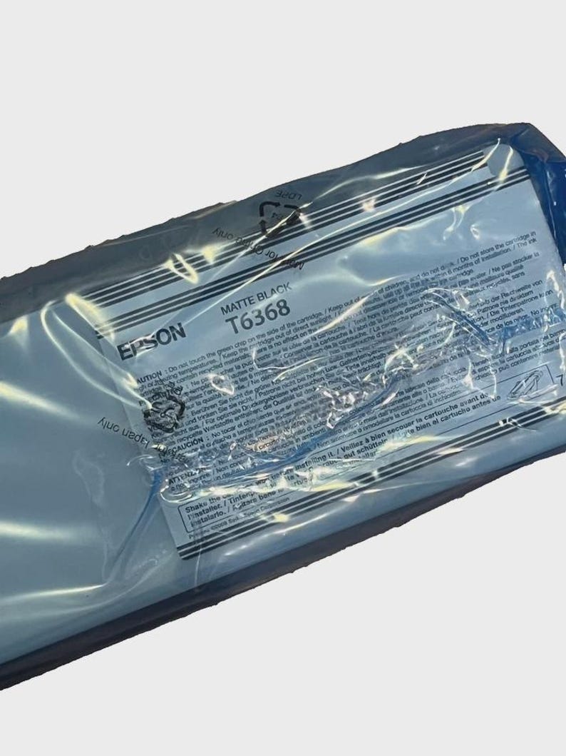 May include: A sealed Epson Matte Black T6368 ink cartridge in a clear plastic package. The package has printed text and warnings in multiple languages. The Epson logo is visible.