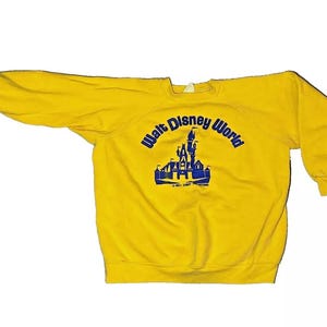 May include: Yellow sweatshirt with a blue graphic of Cinderella's castle and the text "Walt Disney World".