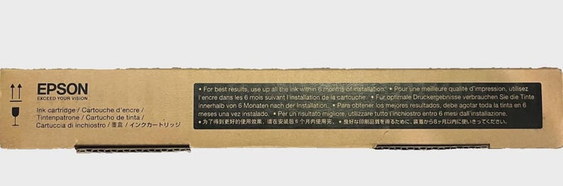 May include: A cardboard box for an Epson ink cartridge. The box has the Epson logo and text in multiple languages. The box also has international shipping symbols and a black label with usage instructions.
