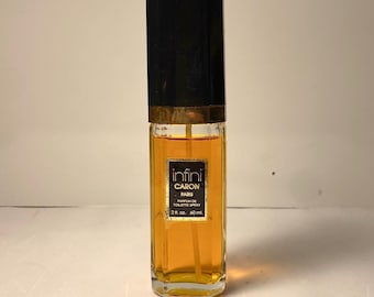 May include: A rectangular perfume bottle with a black cap and gold accents. The bottle contains a golden-colored liquid and has a label that reads "Infini Caron Paris Parfum de Toilette Spray 2 fl. oz. 60 ml."