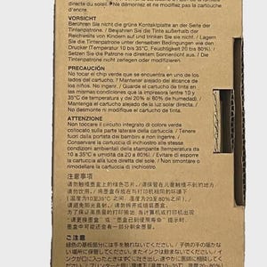May include: A cardboard box with printed warnings in multiple languages about an ink cartridge. The text cautions against touching a green chip, keeping it away from children, and storing it properly. The box also has recycling symbols.