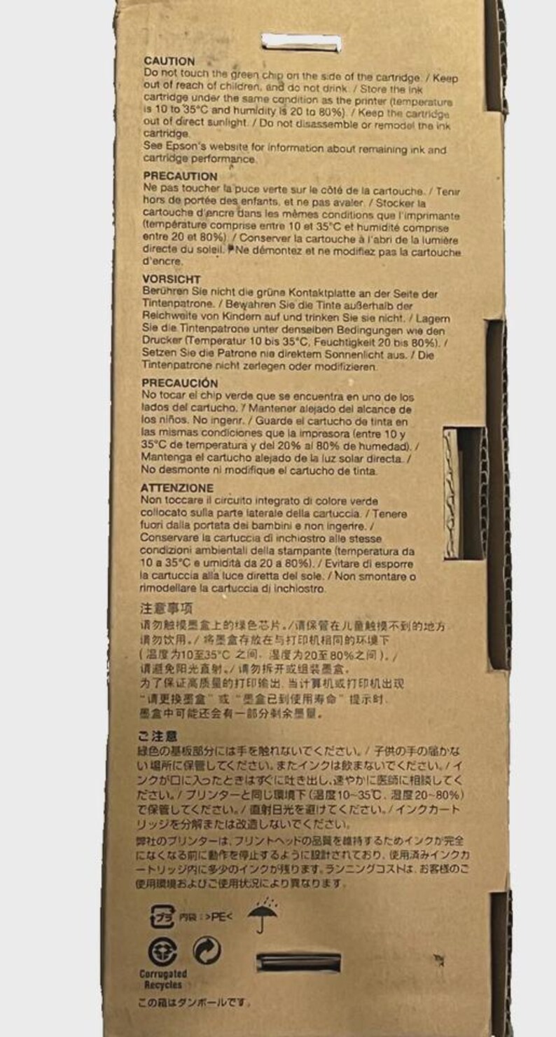 May include: A cardboard box with printed warnings in multiple languages about an ink cartridge. The text cautions against touching a green chip, keeping it away from children, and storing it properly. The box also has recycling symbols.