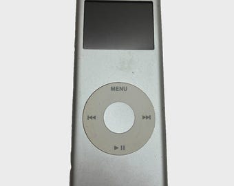 May include: A silver digital music player with a rectangular black screen and a circular navigation click wheel. The click wheel features the word MENU at the top, along with icons for track skipping, play, and pause functions.