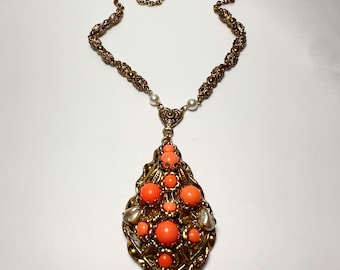 May include: A gold necklace with a large pendant featuring a cluster of orange and white beads. The pendant is ornate and has a detailed design.