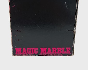 May include: A vintage box with the words "MAGIC MARBLE" in bright pink lettering. The box is black with a pink circle at the top. The text "COPYRIGHT 1971 PATENT APPLIED FOR" is also visible.