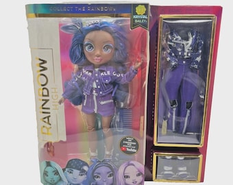 May include: A Rainbow High fashion doll, Krystal Bailey, in a purple outfit, is displayed in a box. The doll has blue hair and is wearing a purple jacket and shorts. The packaging includes the text "COLLECT THE RAINBOW".