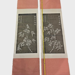 May include: Two vintage Japanese scroll paintings. Each features a black and white bamboo illustration on a white background, with Japanese characters. The scrolls have a pink textured border. The total length is approximately 60 inches.