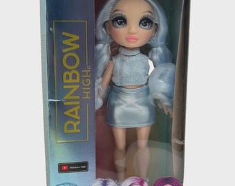 May include: A Rainbow High doll, Gabriella, in a clear plastic box. The doll has pale blue hair, a silver top and skirt. The box reads "LET YOUR TRUE COLORS SHINE" and "RAINBOW HIGH."
