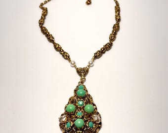 May include: A gold necklace with a teardrop-shaped pendant featuring a cluster of green and clear stones. The pendant is surrounded by small white pearls.