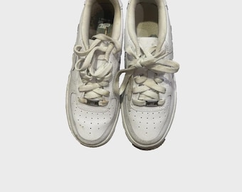 May include: A pair of white leather sneakers with white laces. The shoes have a low-top design with a perforated toe box and a silver metal tag on the laces. The soles are white with a gray trim.