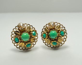 May include: A pair of gold tone earrings with a filigree design. The earrings feature a large green stone surrounded by smaller green stones and a pearl-like accent.
