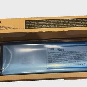 May include: Epson T6362 ink cartridge in a cardboard box. The box is open, revealing the ink cartridge inside a blue plastic wrap. The Epson logo and product information are visible on the cartridge.