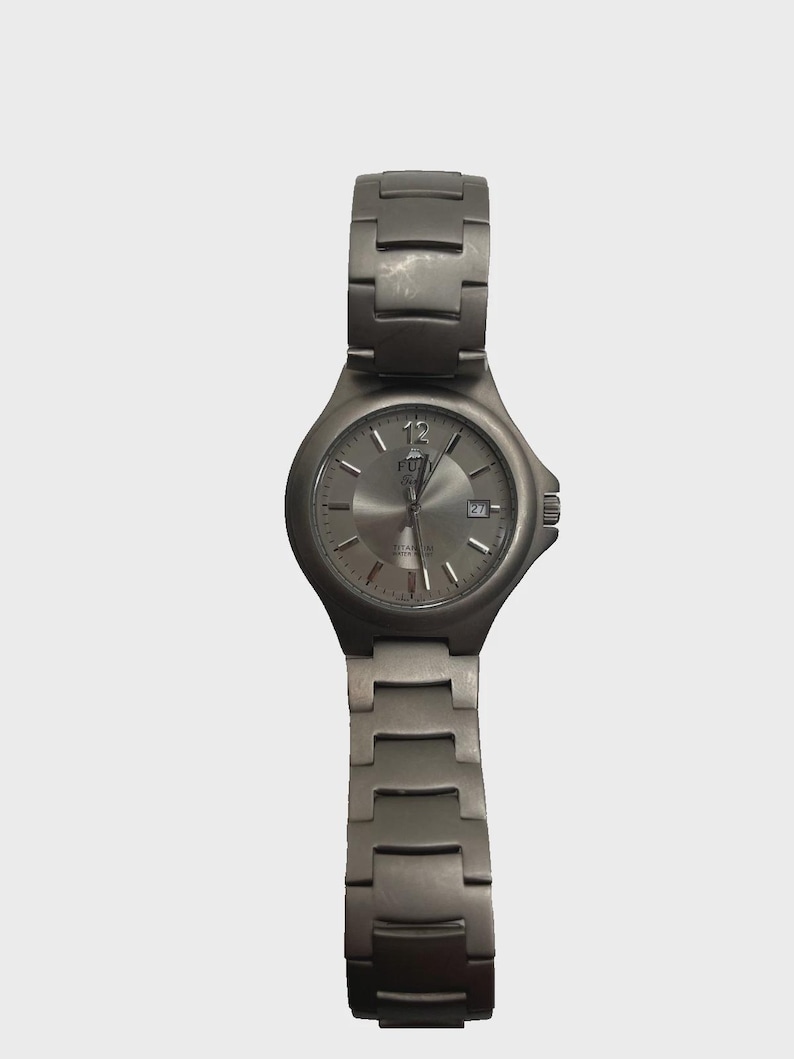 May include: A titanium wristwatch with a silver dial and matching strap. The watch has a date display and luminous hands. The watch is a classic design, suitable for everyday wear. The watch strap is approximately 20 cm long.